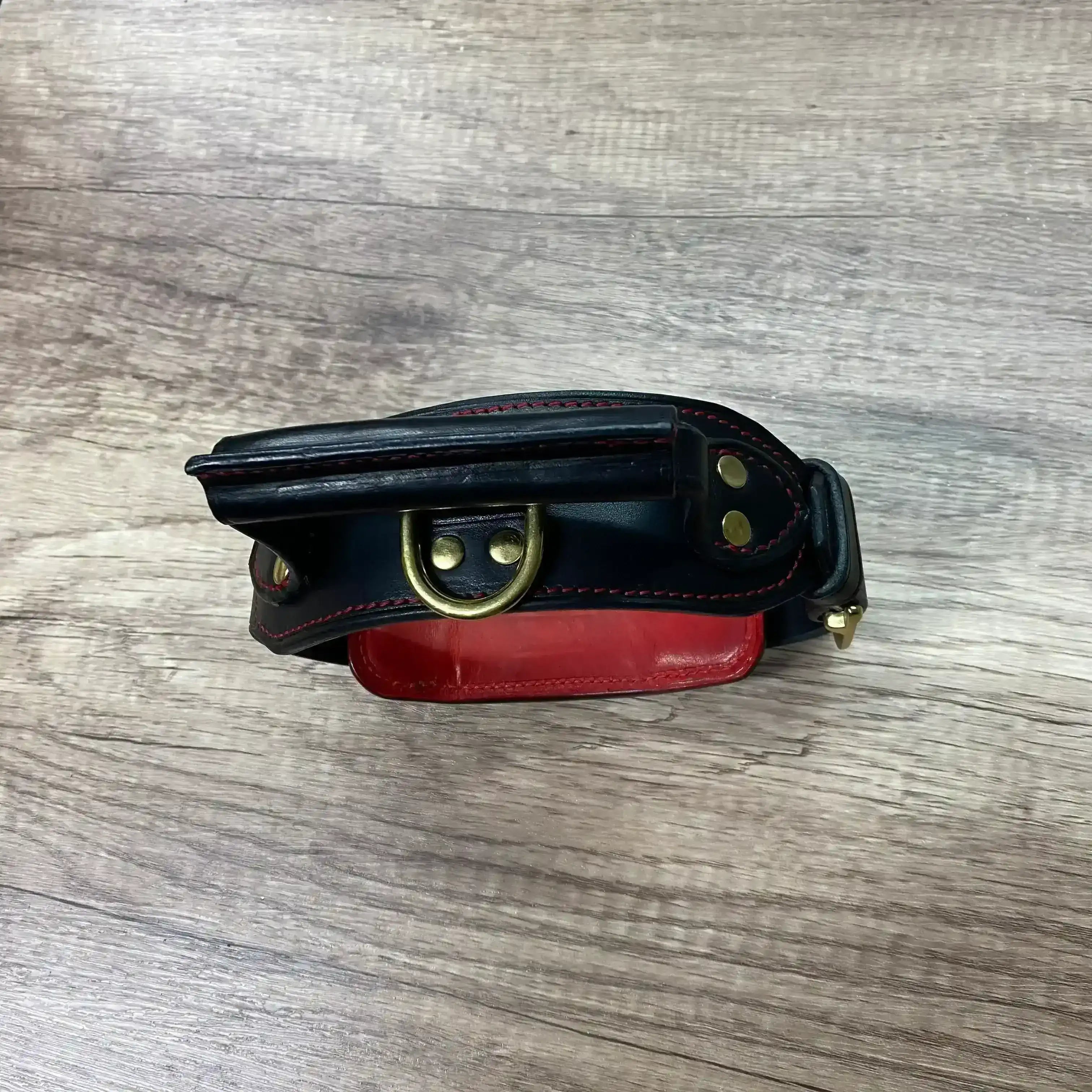 Black leather collar with red interior and gold buckle on a wooden surface