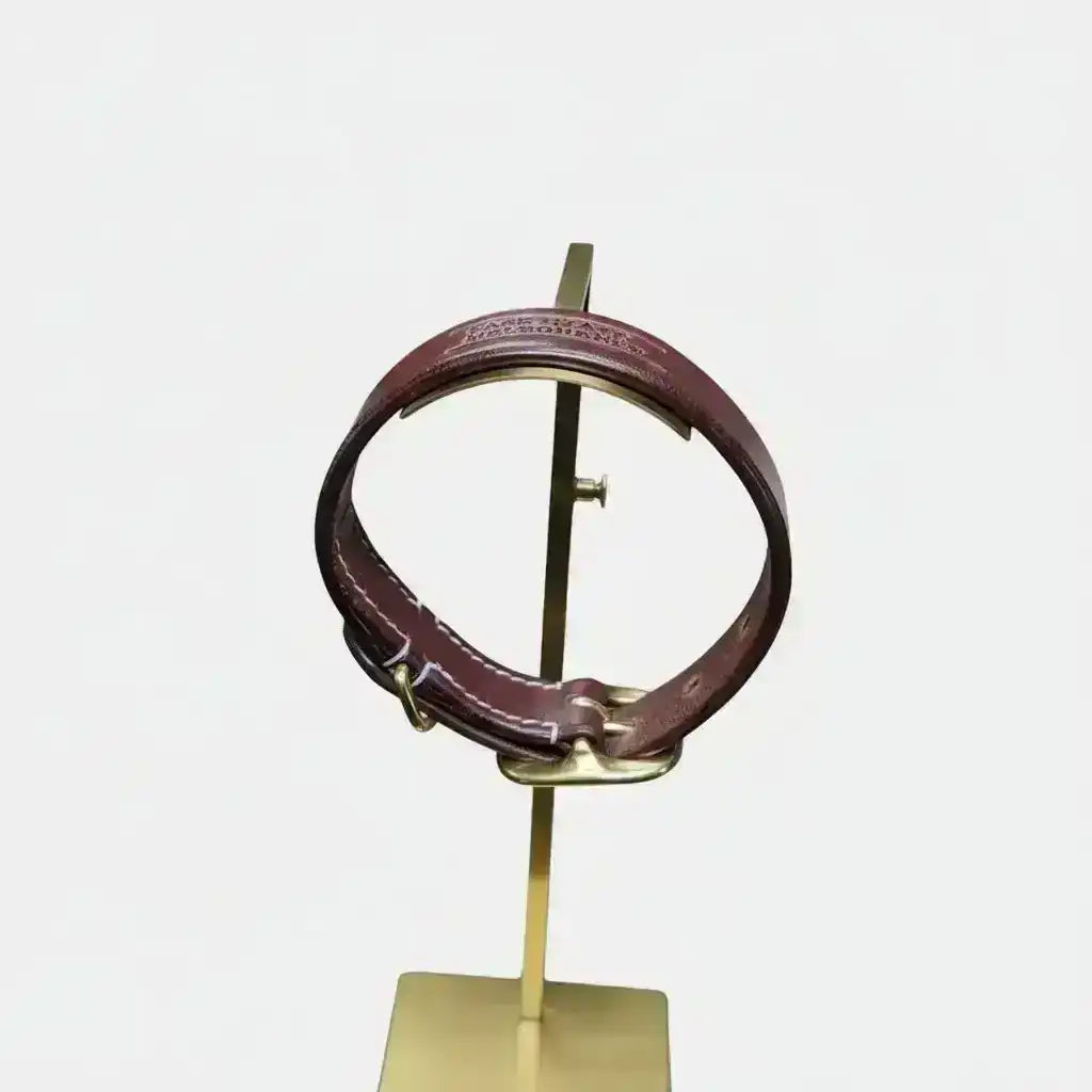 Burgundy leather dog collar with gold hardware on a stand in a workshop setting
