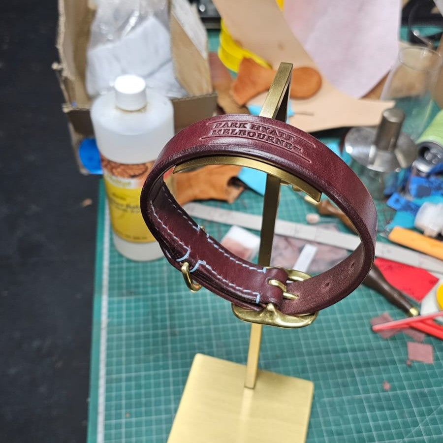 Burgundy leather dog collar with gold hardware on a stand in a workshop setting