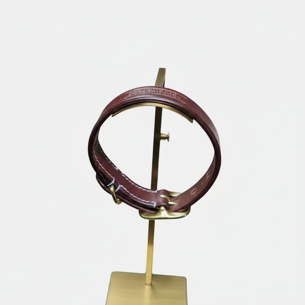 Burgundy leather dog collar with gold hardware on a stand in a workshop setting