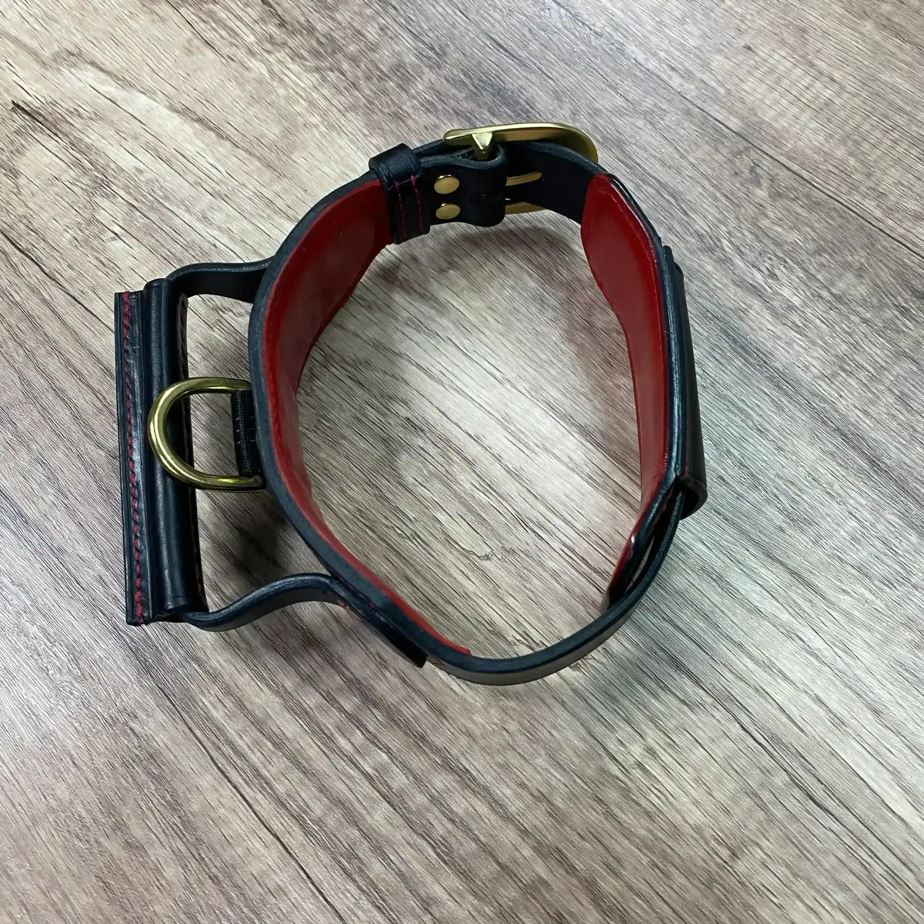 Black leather dog collar with gold hardware on a wooden surface