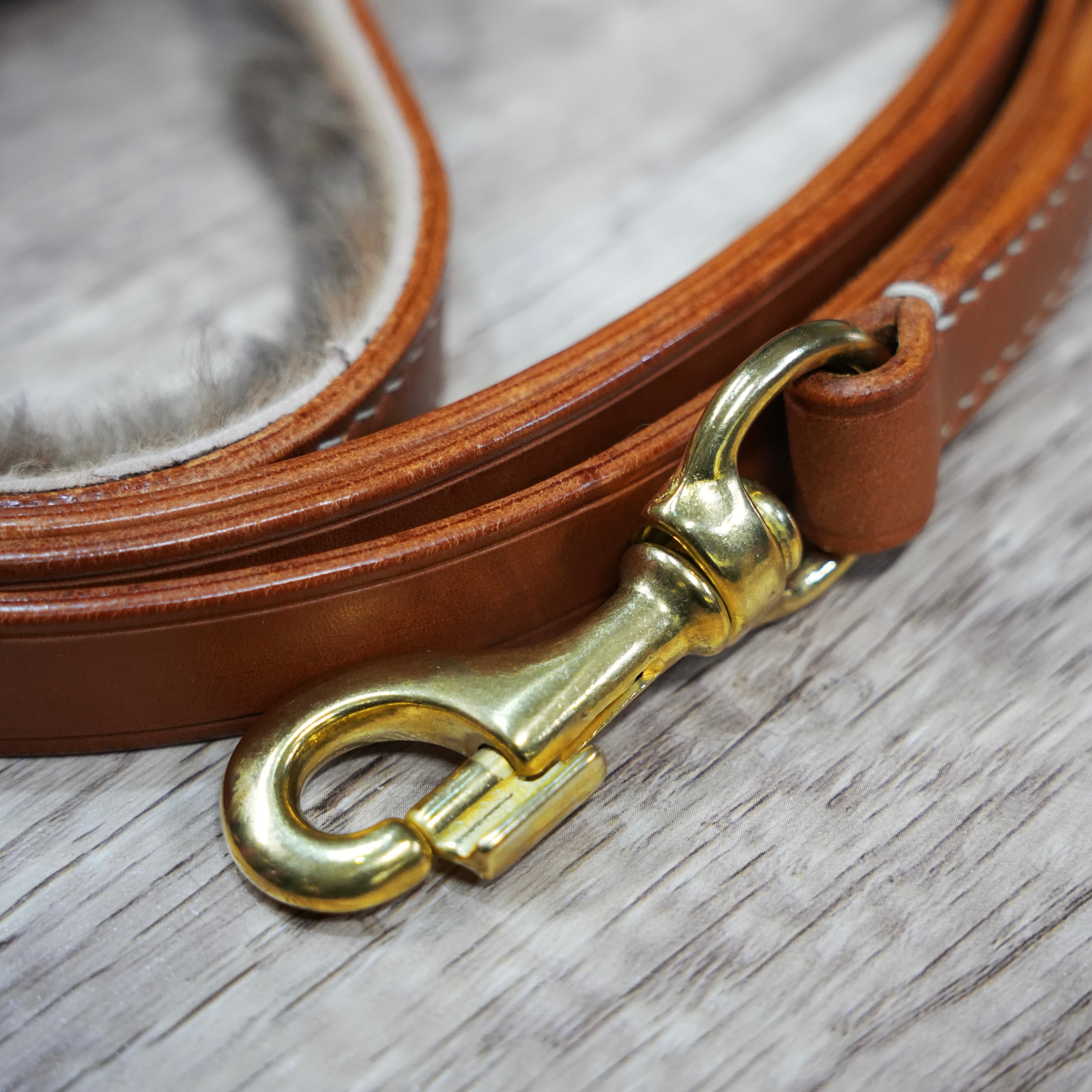 Brown leather dog lead with a brass snap on a wooden surface