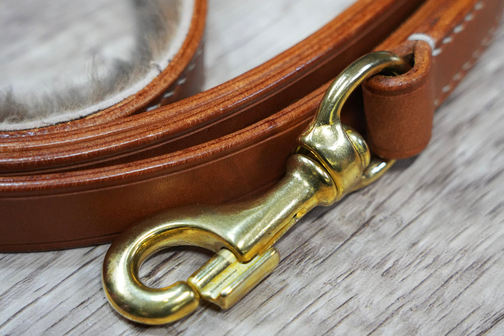 Brown leather dog lead with a brass snap on a wooden surface