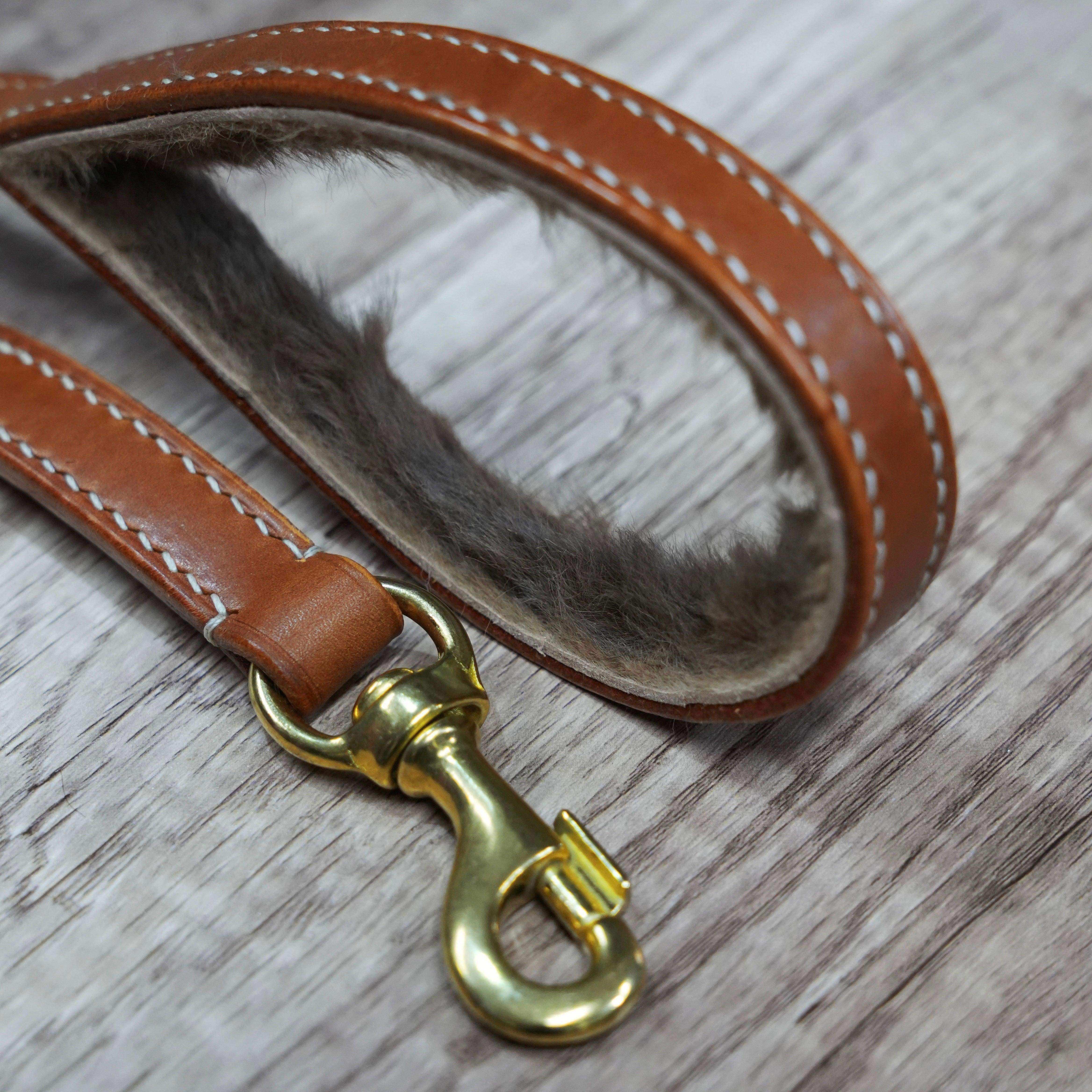 Brown leather dog leash with gold metal clip on a wooden surface